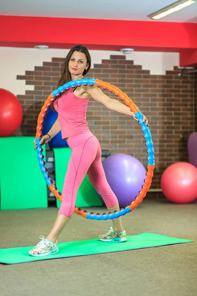 Menina branca bonita nova em um terno de esportes rosa faz exercícios físicos com um aro no centro de fitness . — Fotografia de Stock