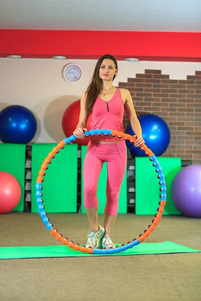 Joven hermosa chica blanca en un traje deportivo rosa hace ejercicios físicos con un aro en el gimnasio . — Foto de Stock