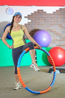 Genç güzel kız bir sarı beyaz ve gri spor takım fiziksel egzersizler fitness merkezinde bir çember ile mu.