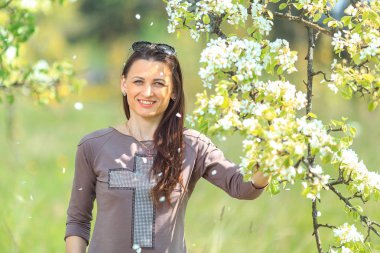 Genç güzel kız bahçede elma ağaçlarının çiçek açması dalları yakınındaki bir kahverengi spor takım elbise standları beyaz.