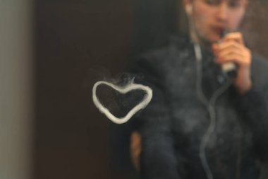 Genç yakışıklı beyaz adamın kalp şeklinde Buhar Yüzükler izin. Vaping.