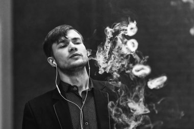 Genç yakışıklı beyaz adam Buhar Yüzükler izin verdi. Vaping. Elektronik sigara. Siyah ve beyaz fotoğraf.