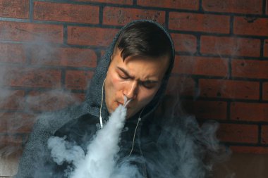 Genç yakışıklı beyaz adam admiting puffs üzerinden elektronik sigara Buhar olduğunu. Vaping. Müzik genç.
