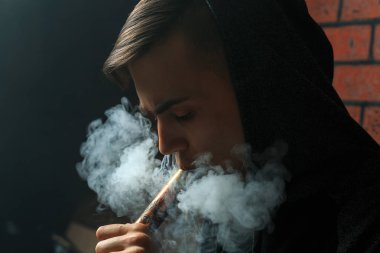 Genç yakışıklı beyaz adam admiting puffs üzerinden elektronik sigara Buhar olduğunu. Vaping. Müzik genç.