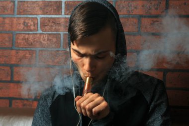 Genç yakışıklı beyaz adam admiting puffs üzerinden elektronik sigara Buhar olduğunu. Vaping. Müzik genç.