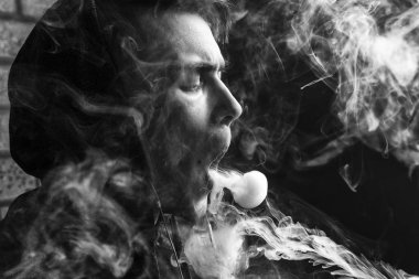 Genç yakışıklı beyaz adam admiting puffs üzerinden elektronik sigara Buhar olduğunu. Vaping. Genç müzik. Siyah ve beyaz fotoğraf.