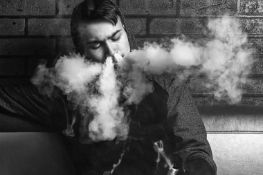 Genç yakışıklı beyaz adam admiting puffs üzerinden elektronik sigara Buhar olduğunu. Vaping. Genç müzik. Siyah ve beyaz fotoğraf.