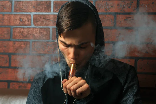 Der junge, gut aussehende weiße Mann bewundert die Dampfschwaden der elektronischen Zigarette. Dämpfen. Teenager hören Musik. — Stockfoto