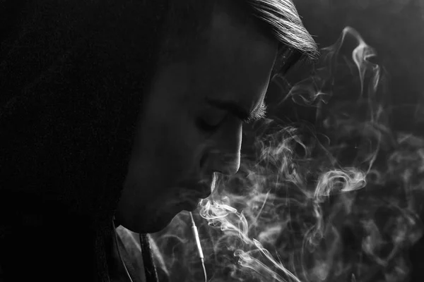 Der junge, gut aussehende weiße Mann bewundert die Dampfschwaden der elektronischen Zigarette. Dämpfen. Teenager hören Musik. Schwarz-Weiß-Foto. — Stockfoto