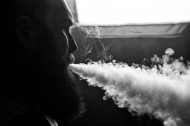 Vape. Büyük sakallı genç yakışıklı beyaz adam admiting puffs üzerinden elektronik sigara Buhar olduğunu. Siyah ve beyaz fotoğraf.