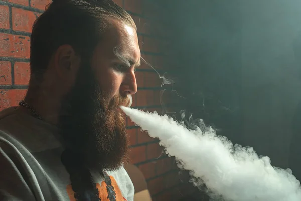 Vape. Jeune homme blanc brutal avec une grande barbe admire les bouffées de vapeur de la cigarette électronique . — Photo