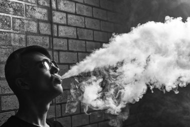 Vape. Genç yakışıklı beyaz güneş gözlüklü elektronik sigara buhar admiting puffs biri. Vaping. Genç müzik. Siyah ve beyaz fotoğraf.