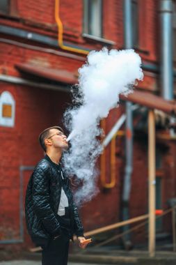Vape. Yakışıklı genç bir beyaz adam buhar bir vintage eski kırmızı bahçesinde elektronik sigara gelen darbeler. Vaping.
