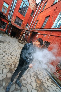 Vape. Yakışıklı genç bir beyaz adam buhar bir vintage eski kırmızı bahçesinde elektronik sigara gelen darbeler. Vaping.