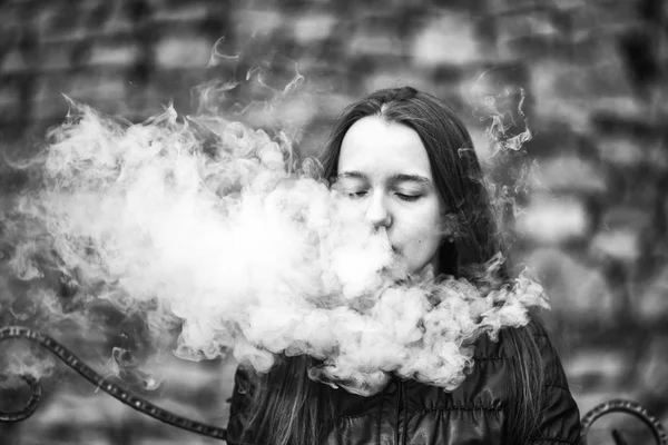 Vape. Uma jovem menina branca bonita está sentada em um banco vintage e está fumando um cigarro eletrônico. Estilo de vida. Foto em preto e branco . — Fotografia de Stock