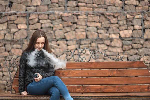 Vape. ein junges schönes weißes Mädchen sitzt auf einer Vintage-Bank und raucht eine elektronische Zigarette. Lebensstil. — Stockfoto