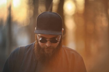 Güneş gözlüklü büyük sakal ve gün batımında ormanda bir kap ile acımasız bir genç adam. Yaşam tarzı.