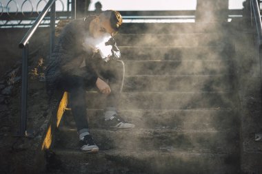 Vape. Genç yakışıklı adam merdivenlerde oturur ve Buhar elektronik sigara darbeler. Yaşam tarzı.