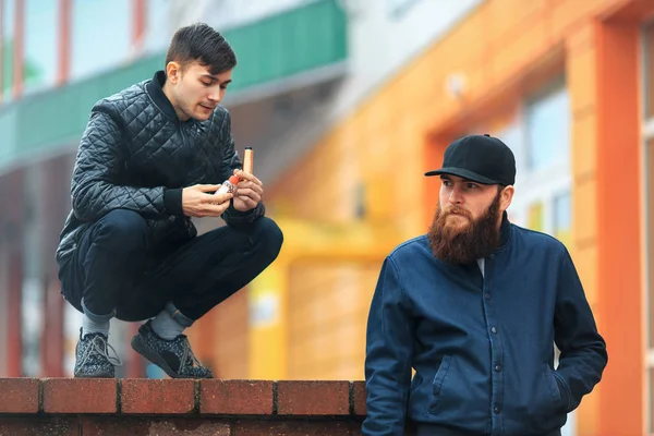 Vape. Two young people stand and smoke electronic cigarettes in the street on a cloudy day.