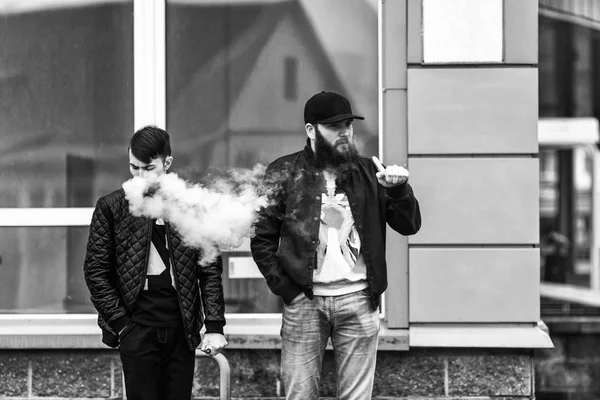 Вэйп. Двое молодых людей стоят и курят электронные сигареты. Черное и белое . — стоковое фото