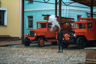 Vape. Genç yakışıklı adam yakınındaki eski itfaiye arabası duruyor ve elektronik sigara buhar kapalı icar.