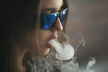 Vape. Genç yakışıklı beyaz güneş gözlüklü elektronik sigara buhar admiting puffs kızdır.