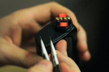 Vape satış sonrası hizmet e-sigara. Erkek el elektronik sigara bobinleri pincette ile düzenler. Parlak sarmal arka plan için. Yakın çekim.