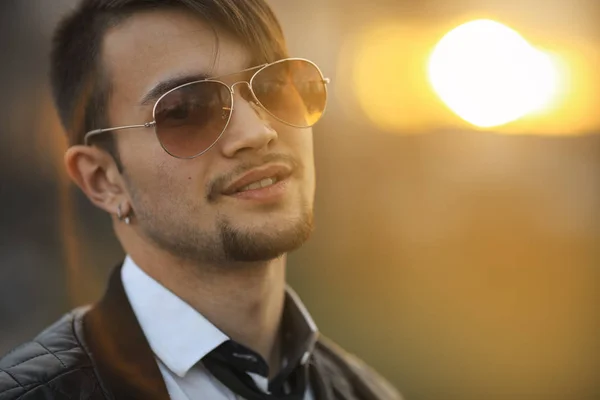 Ora d'oro in primavera. Portret di un bel giovane ragazzo bianco con taglio di capelli moderno in aviatore occhiali da sole in posa al tramonto . — Foto Stock