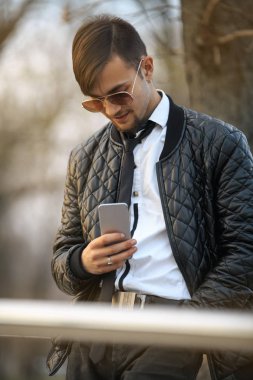 Cep telefonu Gadget adam. Havacı güneş gözlüğü günbatımında smartphone ile poz içinde modern saç kesimi ile yakışıklı bir genç beyaz adamın Portret.