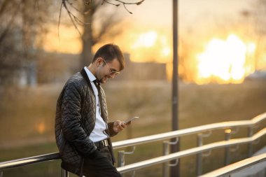 Cep telefonu Gadget adam. Havacı güneş gözlüğü günbatımında smartphone ile poz içinde modern saç kesimi ile yakışıklı bir genç beyaz adamın Portret.