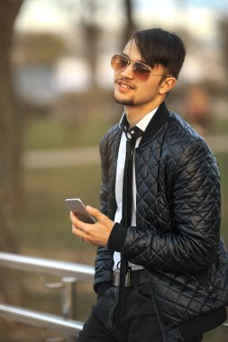 Cep telefonu Gadget adam. Havacı güneş gözlüğü günbatımında smartphone ile poz içinde modern saç kesimi ile yakışıklı bir genç beyaz adamın Portret.