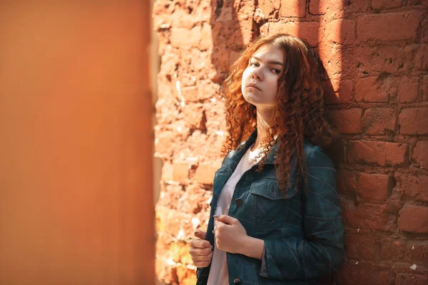 Внешний портрет красивой молодой белой девушки с рыжими кудрявыми волосами и длинными ногами, позирующими на старинном красном кирпичном дворе . — стоковое фото