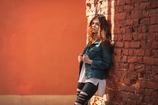 Outdoor Portret van een mooie witte meisje met rood, krullend haar en lange benen poseren in een vintage oude rode bakstenen werf. — Stockfoto