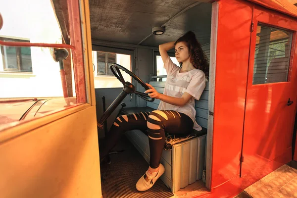 Camião de combate a incêndios vintage e adolescente bonito. Retrato ao ar livre de uma bela jovem menina branca com cabelo encaracolado vermelho e em jeans preto ragged posando ao volante do antigo motor de incêndio . — Fotografia de Stock