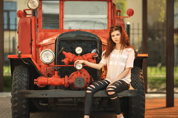 Винтажный пожарный грузовик и симпатичный подросток. Внешний портрет красивой молодой белой девушки с рыжими кудрявыми волосами и в черных рваных джинсах, позирующих возле старой пожарной машины . — стоковое фото