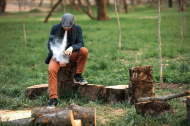 Vape adam. Acımasız bir fotoğrafı genç adam geri kalan chop yakacak odun ve vaping sonra köyde elektronik sigara sahip sakallı.