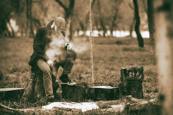 Vaporizzatore. Foto di un giovane barbuto brutale che si riposa dopo aver tagliato la legna e vaporizzato una sigaretta elettronica nel villaggio. Tonica . — Foto Stock