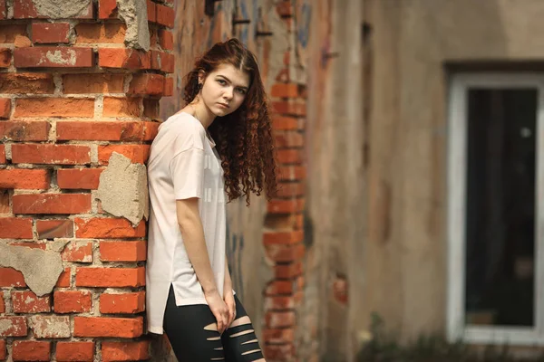 Mooie tiener. Outdoor Portret van een vrij wit meisje met rood krullend haar poseren in de buurt van oude vernietigde rode bakstenen muur. — Stockfoto