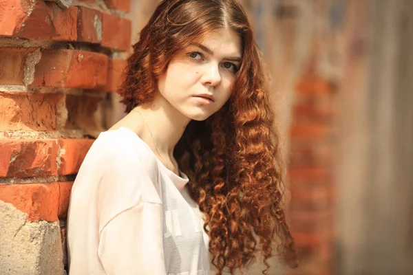 Прекрасный подросток. Внешний портрет красивой молодой белой девушки с рыжими вьющимися волосами, позирующими возле старой разрушенной стены из красного кирпича . — стоковое фото