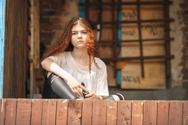 Mooie vape tiener. Portret van een mooie jonge witte meisje met rood krullend haar vaping een elektronische sigaret in de buurt van de oude verwoeste dorpshuis. — Stockfoto