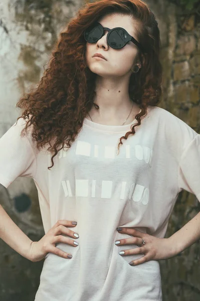 Mooie tiener. Outdoor Portret van een vrij wit meisje met rood krullend haar in zonnebril poseren in de buurt van oude vernietigde rode bakstenen muur. Toned. — Stockfoto
