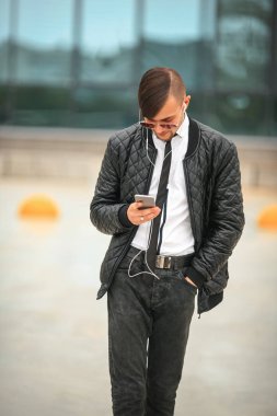 Portret havacı güneş gözlüğü içinde modern saç kesimi ile yakışıklı genç bir beyaz adam ve kulaklık ile şehir arka plan karşısında hareket eden telefon.