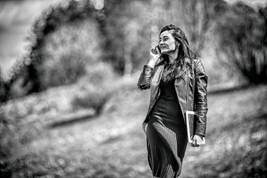 Gadget'ı kadın. Genç güzel beyaz kız siyah saçlı ve cep telefonda konuşurken ve bir tablet elinde tutan siyah giysili portresi. Siyah ve beyaz fotoğraf.