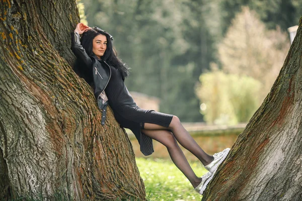 Портрет молодої красивої білої дівчини з чорним волоссям і в чорному одязі, що позує біля старого дерева . — стокове фото