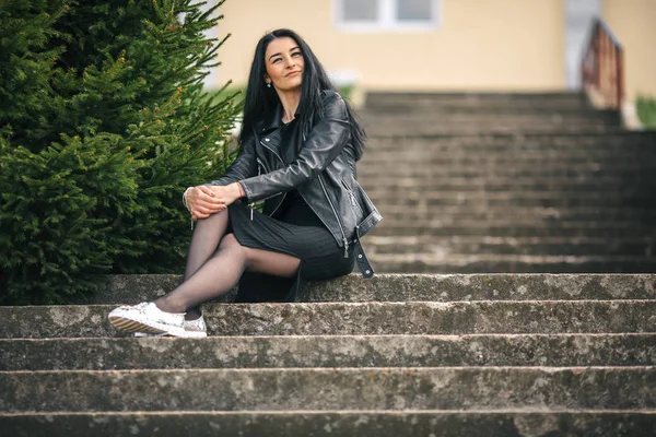 Retrato de menina branca bonita nova com cabelo preto e em roupas pretas sentadas na escada de pedra velha . — Fotografia de Stock