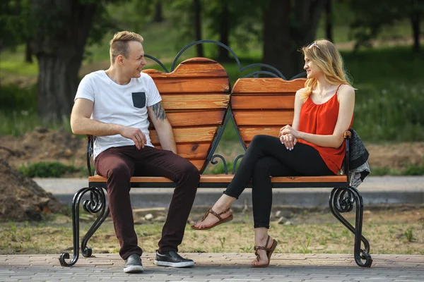 Young couple falling in love on the bench in the form of hearts in the city park at summer day.