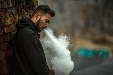 Vape adam. Fotoğraf siyah elbiseli vaping ve eski yakınındaki elektronik sigara buhar kapalı icar modern saç kesimi ile yakışıklı bir genç beyaz adamın kırmızı tuğla duvar yıkıldı. Yaşam tarzı.