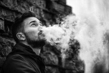 Vape adam. Fotoğraf siyah elbiseli vaping ve eski yıkılan tuğla duvar yakınındaki elektronik sigara buhar kapalı icar modern saç kesimi ile yakışıklı genç bir beyaz adam. Siyah ve beyaz fotoğraf.