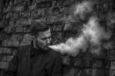 Vape adam. Siyah elbiseli vaping ve elektronik sigara buhar kapalı icar modern saç kesimi ile yakışıklı genç bir beyaz adam fotoğrafı