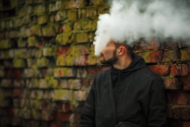 Vape adam. Siyah elbiseli vaping ve elektronik sigara buhar kapalı icar modern saç kesimi ile yakışıklı genç bir beyaz adam fotoğrafı